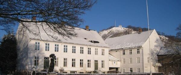 Bildet viser Andorsengården, Mandal museum, en fin vinterdag med små på taket og på bakken. I bakgrunnen ses utsiktspunktet Uranienborg.