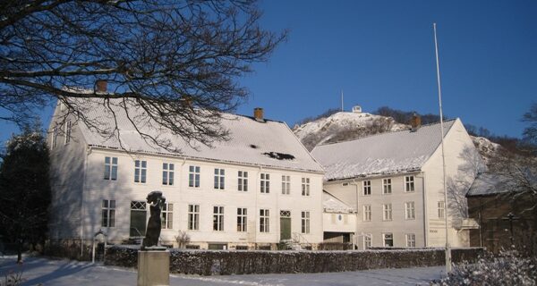Bildet viser Andorsengården, Mandal museum, en fin vinterdag med små på taket og på bakken. I bakgrunnen ses utsiktspunktet Uranienborg.