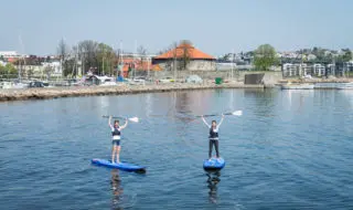 To personer på SUP-brett med Kristiansand festning i bakgrunnen.