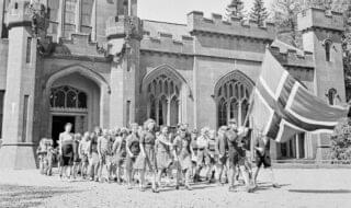 I et gammelt slott i Skottland er en norsk pensjonatskole blitt opprettet. Naturen deroppe likner meget på Norges, og både lærere og elever føler seg hjemme i dette miljø. Undervisningen på skolen som har ca. 70 elever er lagt så nær opp til det pensum som blir krevet på norske skoler. Eleverne har hver sin liten jordflekk hvor de dyrker grønnsaker og blomster. Med det norske flagget i spissen marsjerer elevene ut på gårdsplassen. London, juli, 1943.