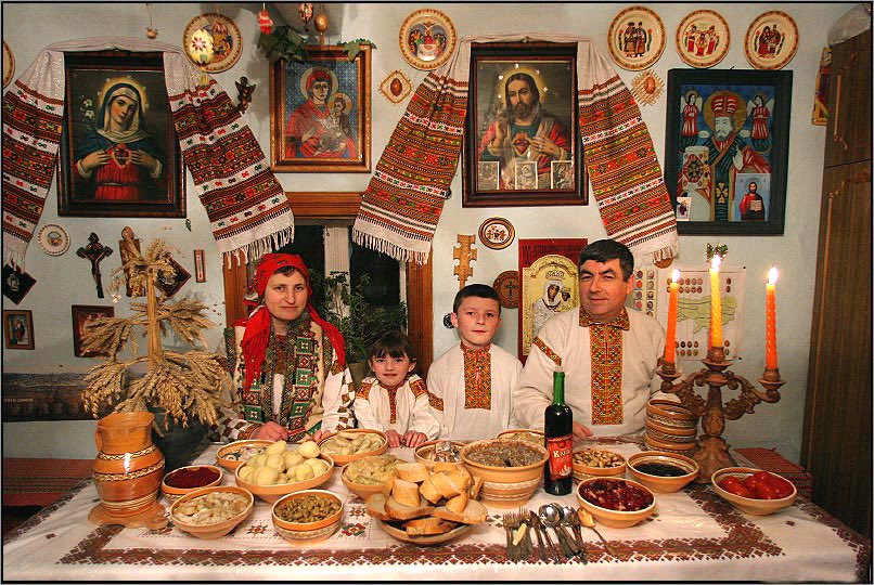 Festkledd ukrainsk familie samlet til julemåltid med didukh på bordet og ikoner på veggen