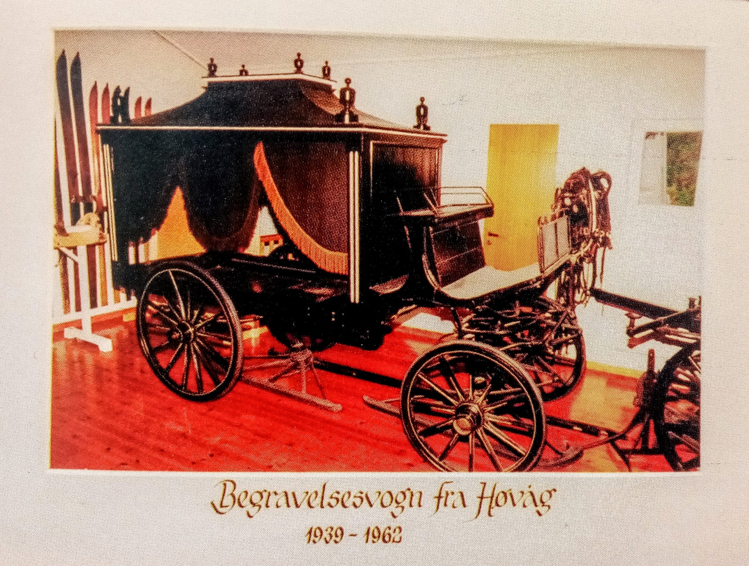 Bilde fra en bok eller brosjyre som viser bårevogna utstilt i vognhallen på fylkesmuseet