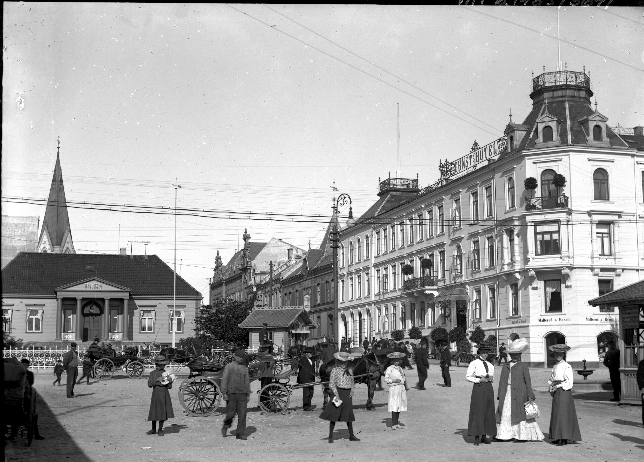 Folk og hestevogner foran Børsparken der kiosken står på hjørnet, til høyre ser man Ernst hotell.