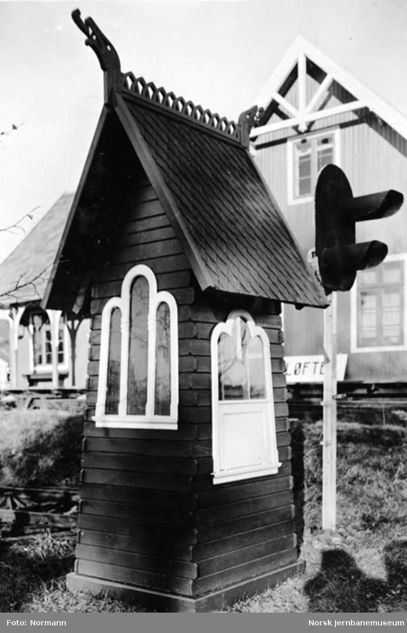 Liten kvadratisk kiosk med skrått tak som en stavkirke. På taket er det et dragehode over hvert møne.