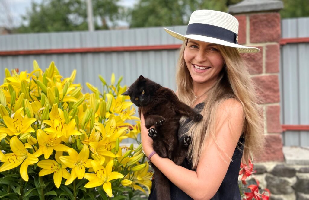 Yuliia Bahniuk glad med svart katt foran gule liljer