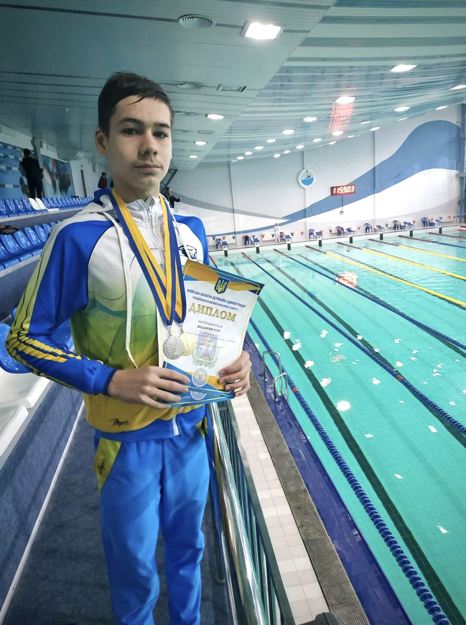 Gutt ved svømmebasseng med medalje og diplom