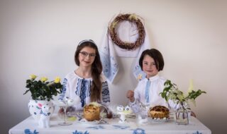 To jenter sitter ved et påskepyntet bord, kledd i tradisjonelle, broderte skjorter fra Ukraina