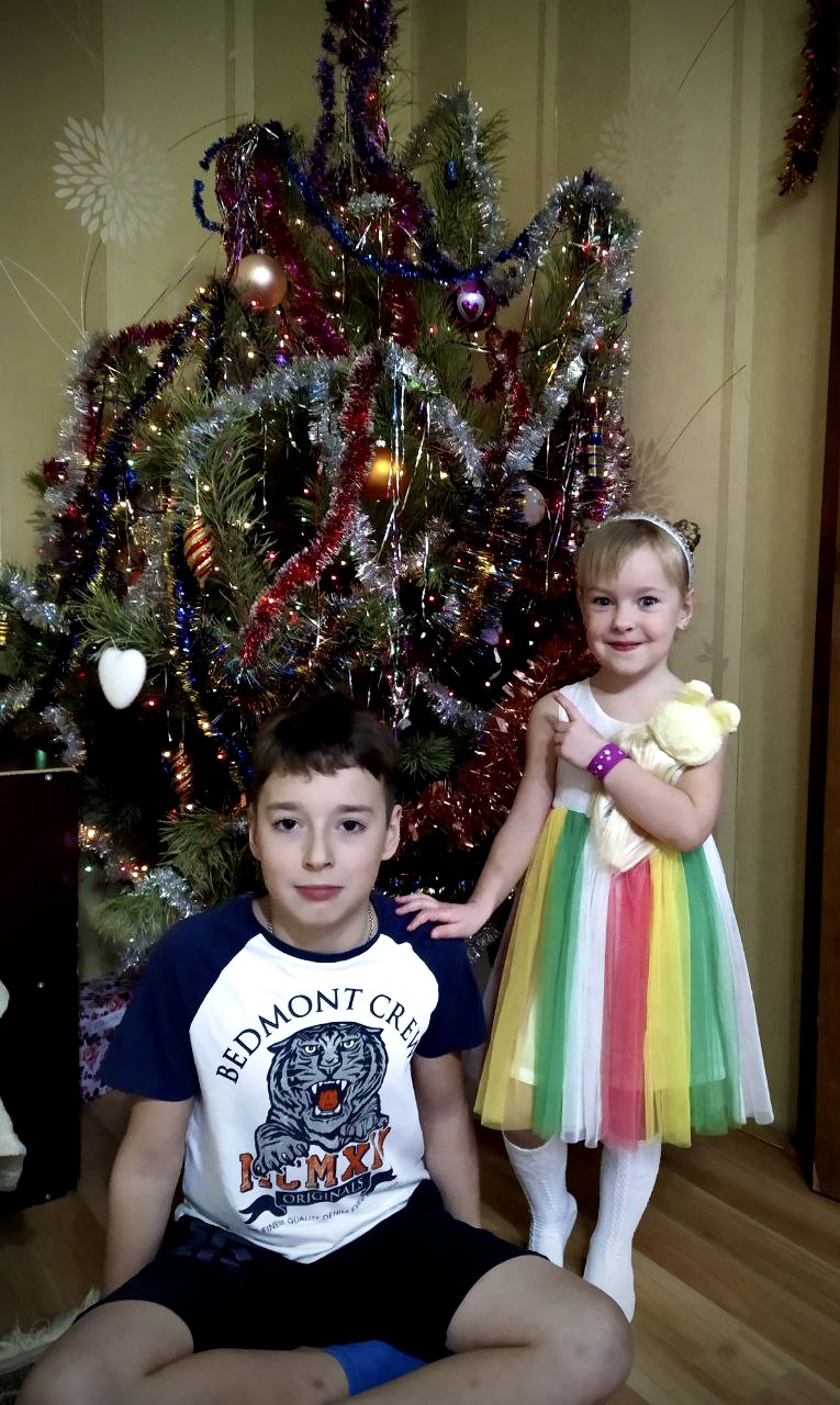 Jente og gutt foran et juletre. De ser glade ut