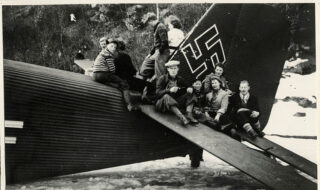 Flystyrten på Fosselandsheia. Voksne og barn sitter på halevingen på et Junkers 52, transportfly. Flyet har nødlandet/styrtet på islagt vann.