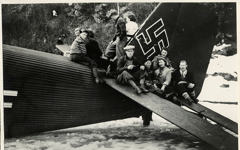 Flystyrten på Fosselandsheia. Voksne og barn sitter på halevingen på et Junkers 52, transportfly. Flyet har nødlandet/styrtet på islagt vann.
