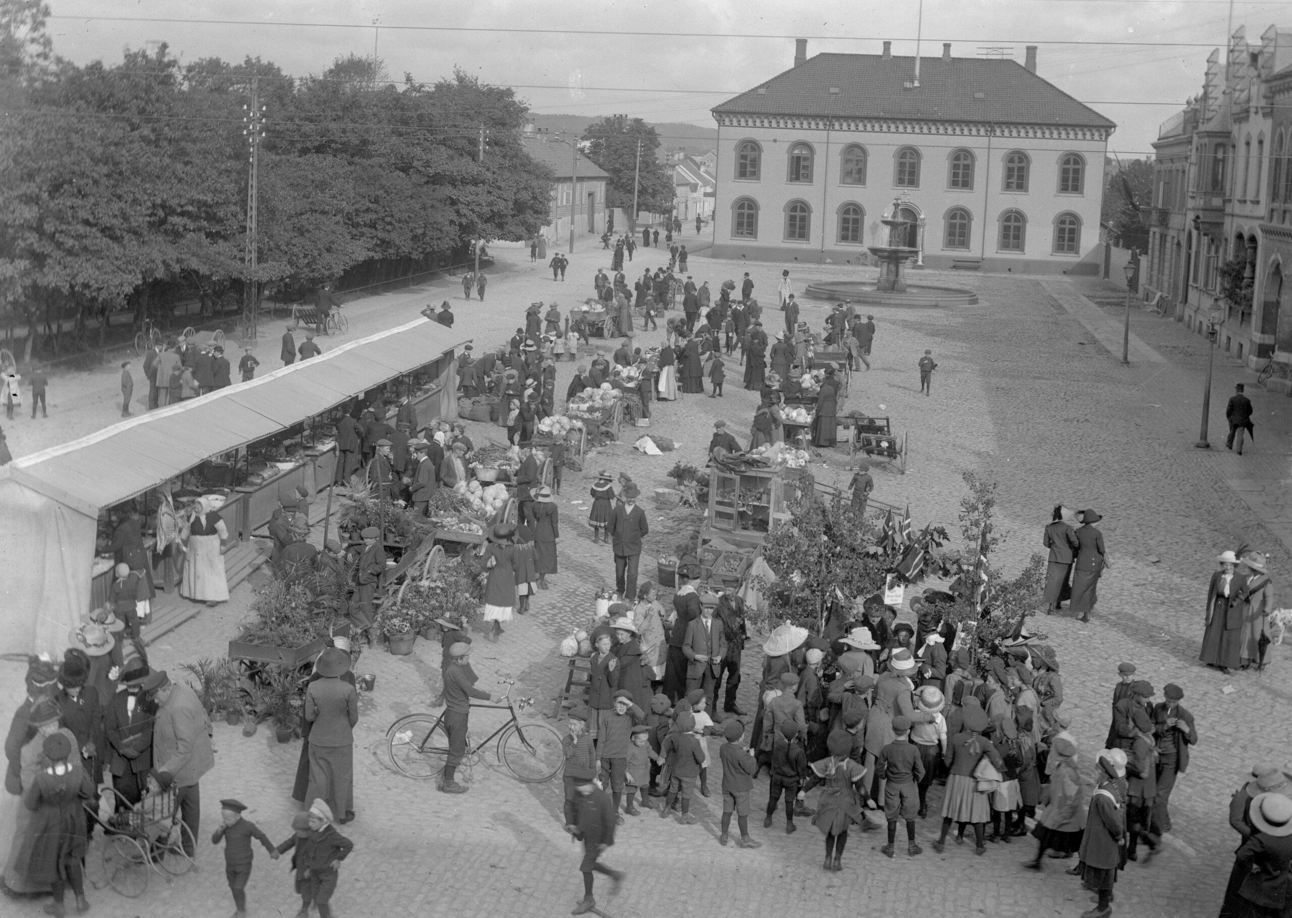 Bildet er i svart-hvitt og viser et mylder av mennesker som handler og prater sammen på torvet. Det er folk i alle aldere der. Ut fra klær og stil er bildet tatt cirka 1915. 