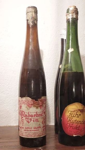 Tre flasker med gamle etiketter og mørkt innhold. De ene er merket Gimle Gård, ved siden av vinflaske fra Fuhrs