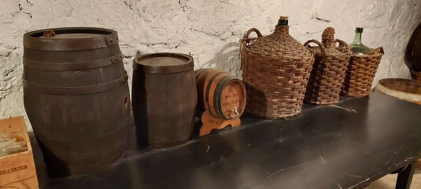 Hylle med to stående tønner, en liten liggende og tre vinballonger, det vil si kurver med store glassbeholdere