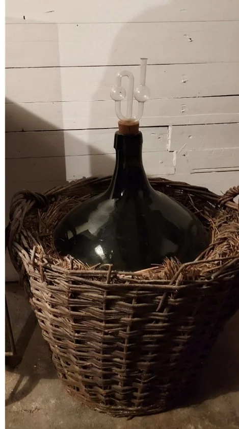 Kurv med stor, bred og mørk glassflaske inni, en vinballing
