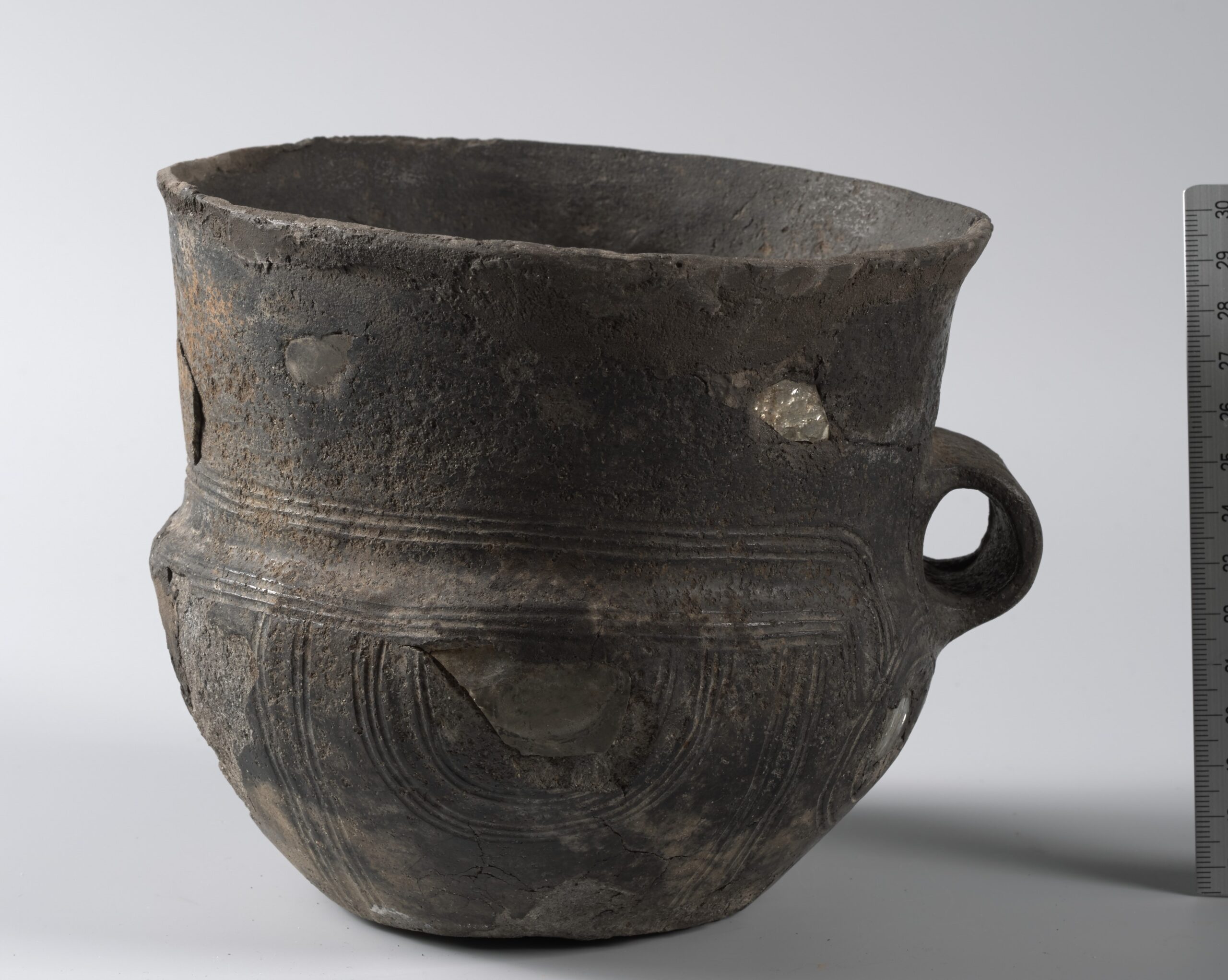 Vindusurne (C. 5767) av keramikk funnet i en gravhaug på Vemestad i Kvås, Lyngdal, rundt 1866. Det som skiller denne urnen fra andre hankeurner er at den har 11 glassbiter fra et knust glassbeger satt inn som små «vinduer» - derav navnet vindusurne. Foto: Kirsten Helgeland, Kulturhistorisk museum i Oslo.