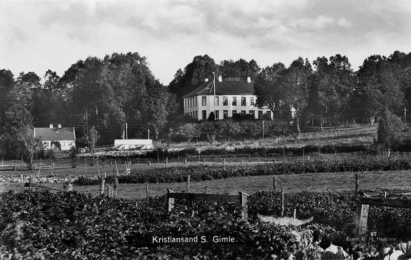Svart-hvitt fotografi med jorder og hager og et stort, hvitt hus i bakgrunnen