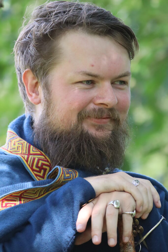 Samuel Høiland står med blå drakt, som er dekorert av bred brikkebånd fra Øvre Berge i Lyngdal.