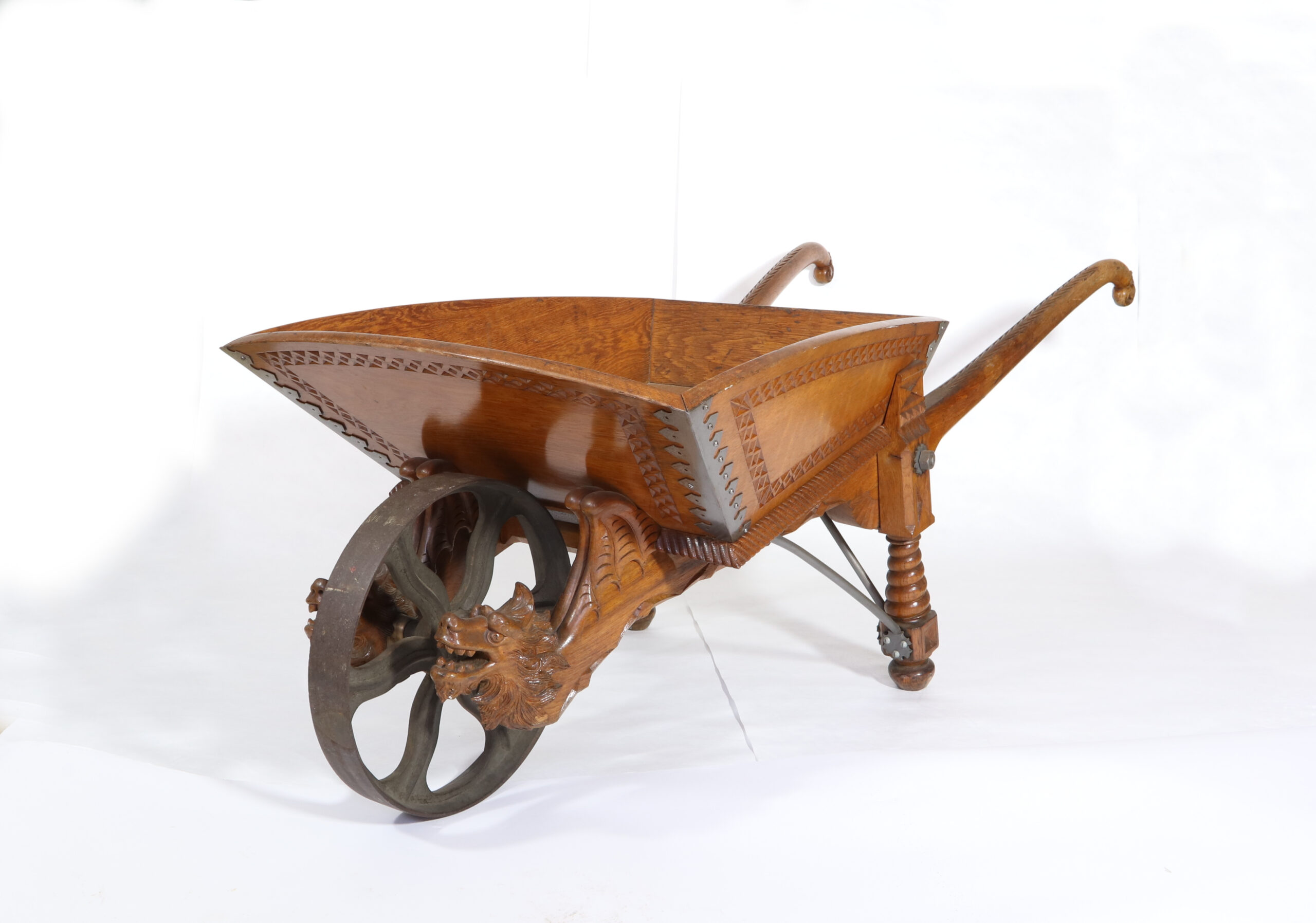 Trillebår i lakkert tre, rikt dekorert med utskjæringer, blant annet løvehoder på hjulakslingen